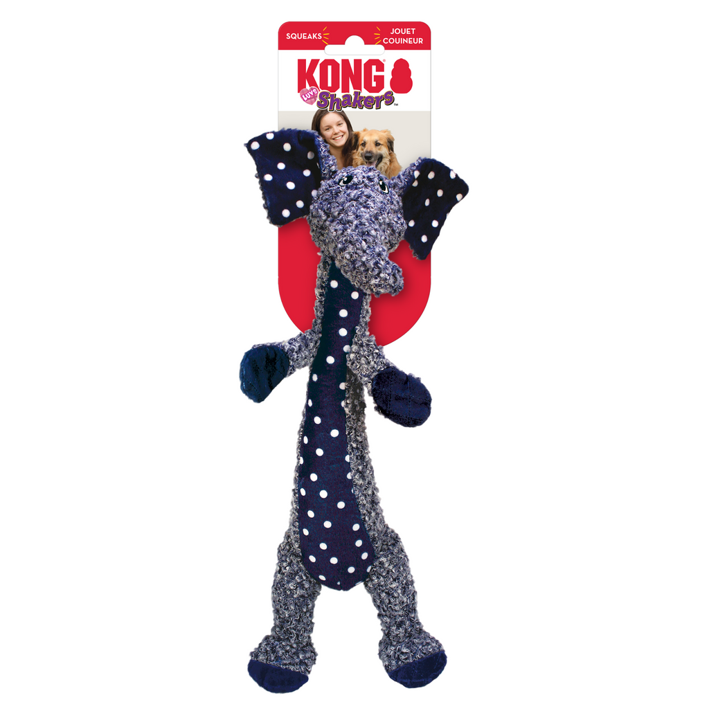 A plush dog toy resembling an elephant with a long trunk, made of a multicolor fabric, including blue and purple, with a squeaker inside. The toy is packaged on a red and white cardboard backing, with a picture of a dog and a person in the background.