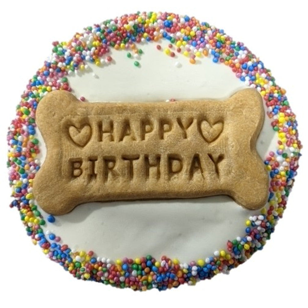 Dog birthday cake with a bone-shaped cookie and 'Happy Birthday' text, surrounded by colorful sprinkles.