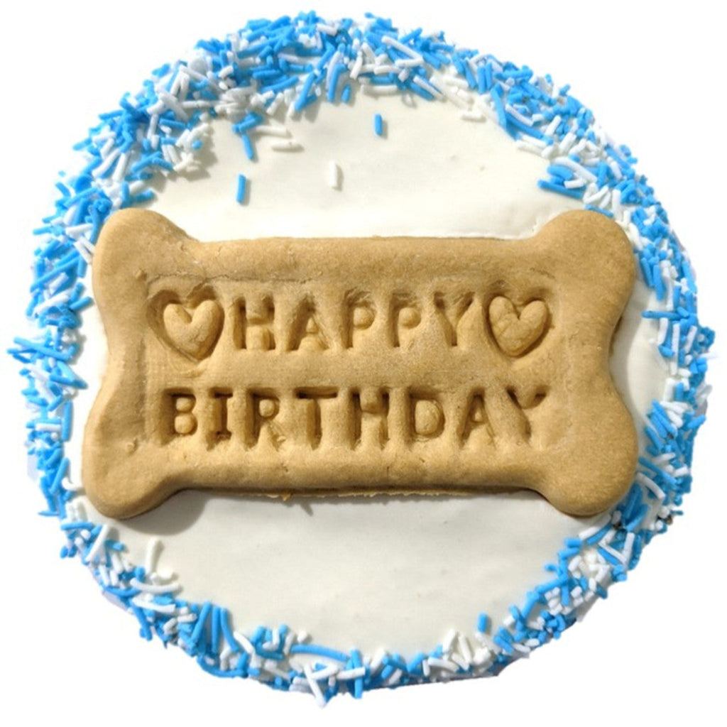 A frosted birthday cake for dogs with 'Happy Birthday' text and blue sprinkles on a white background.
