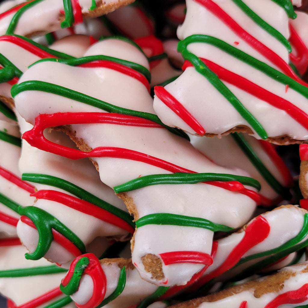 A pile of bone-shaped, candy cane striped dog treats with red, green, and white color scheme, coated in a low-fat yogurt frosting.