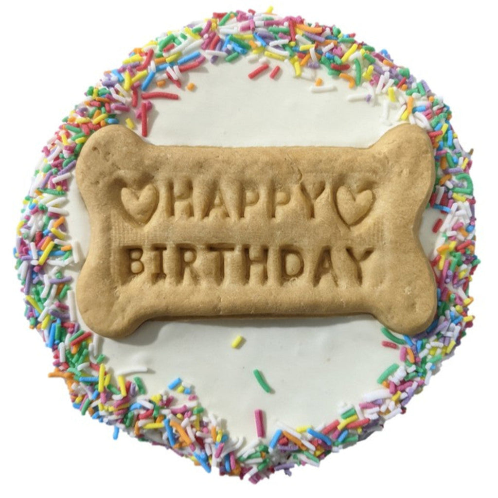 Dog birthday cake with bone-shaped 'Happy Birthday' cookie and colorful sprinkles on a white background